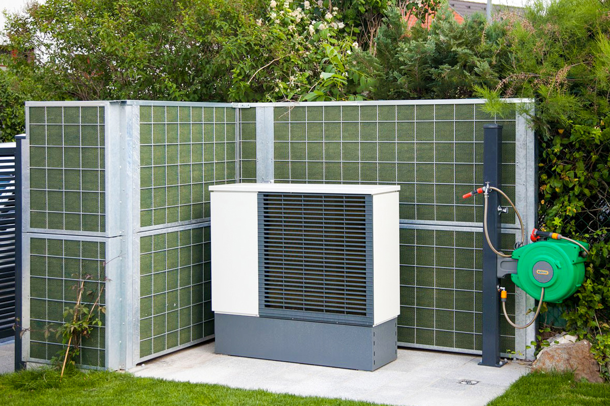 on site air source heat pump in a garden with an open acoustic barrier around the pump to reduce noise.