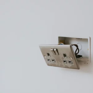 plain plastered wall in a house with UK electric socket hanging off the wall exposing the boxing and wires.