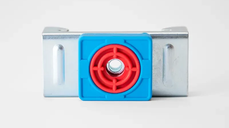 Single MuteClip wall isolatiopn clip for soundproofing. Metal clip with a blue and red dual density silicone. Clip laying on the side.