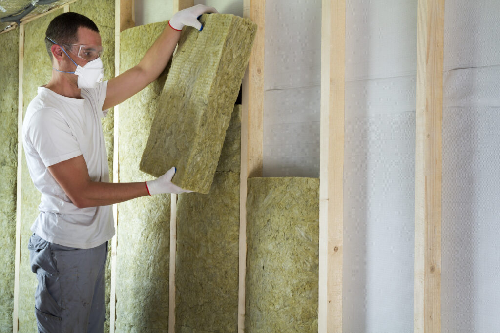 man installtion acoustic mineral wool into a stud wall wearing PPR goggles, gloves and a mask